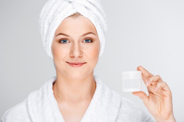Ładna blond kobieta z kąpielowym ręcznikiem na włosy pokazuje śmietankę