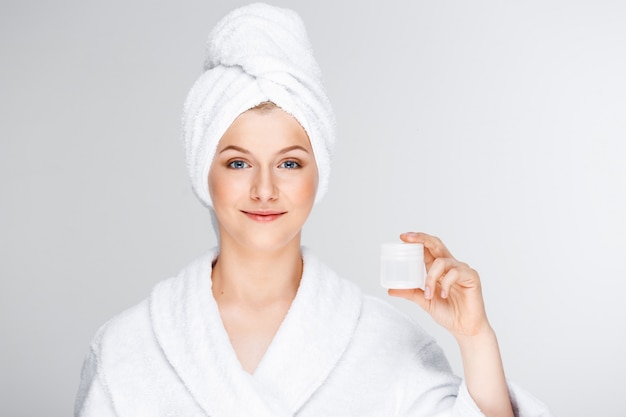 Ładna blond kobieta z kąpielowym ręcznikiem na włosy pokazuje śmietankę