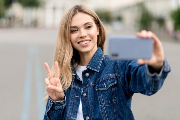 Ładna blondynka biorąc znak pokoju selfie