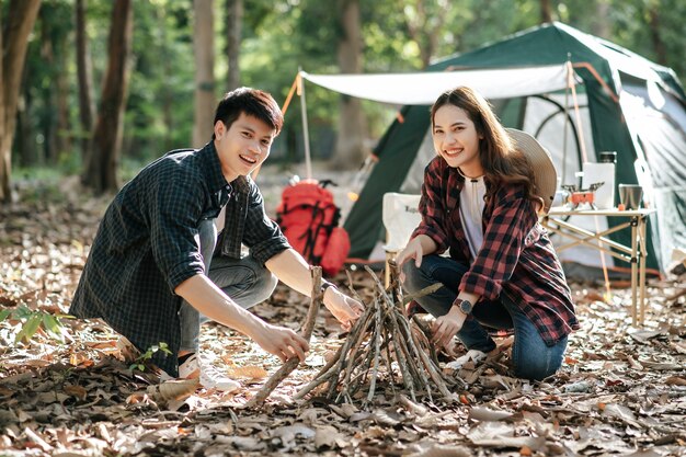 Ładna dziewczyna camper przygotowuje drewno opałowe z chłopakiem, aby rozpalić ognisko. Młoda para turystów pomaga zrywać gałęzie i składać je przed namiotem kempingowym