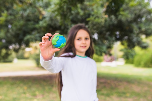 Ładna dziewczyna pokazuje glinianą kuli ziemskiej pozycję w parku