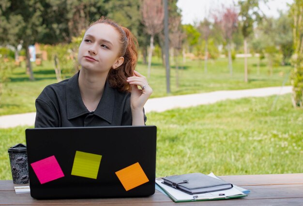 Ładna freelancerka pracująca przy laptopie, patrząca w górę, myśląca, biorąc pod uwagę