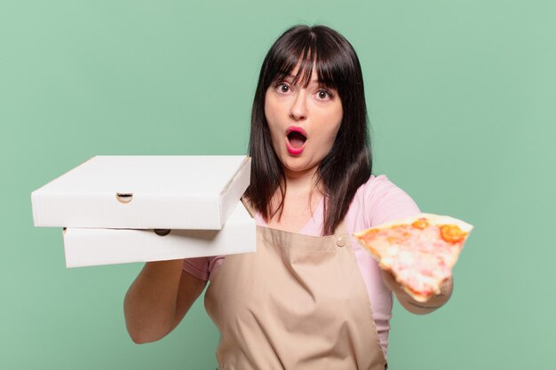 Ładna kobieta szefa kuchni przestraszona wyrazem twarzy i trzymająca pizzę
