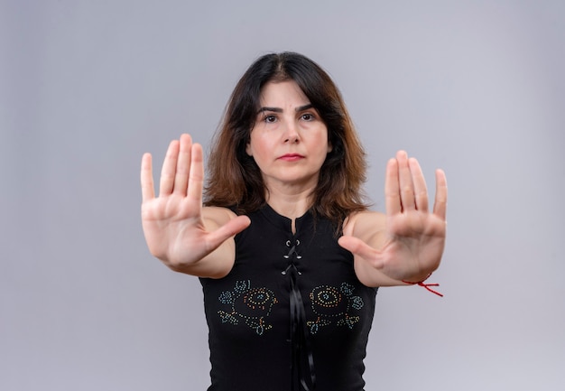 Bezpłatne zdjęcie Ładna kobieta ubrana w czarną bluzkę poważnie pokazuje znak stop rękami