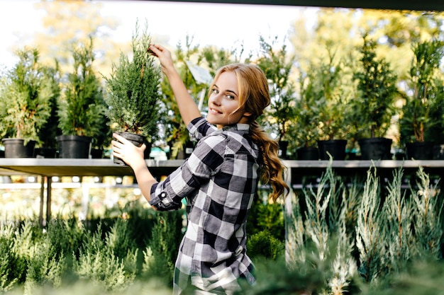 Bezpłatne zdjęcie Ładna kobieta w ślicznych ubraniach sięgająca po rośliny w szklarni