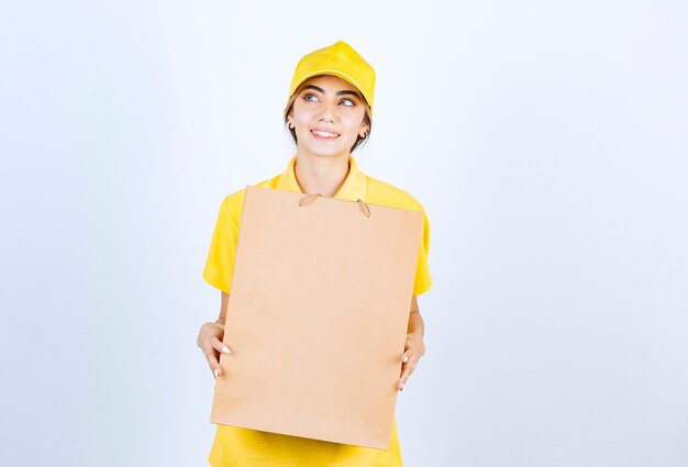 Ładna kobieta w żółtym mundurze trzyma brązową pustą papierową torbę rzemieślniczą.