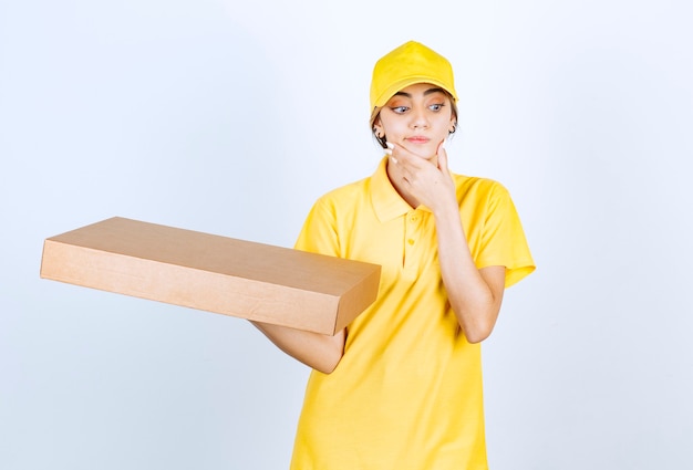 Ładna kobieta w żółtym mundurze trzyma brązowe puste pudełko z papieru rzemieślniczego.