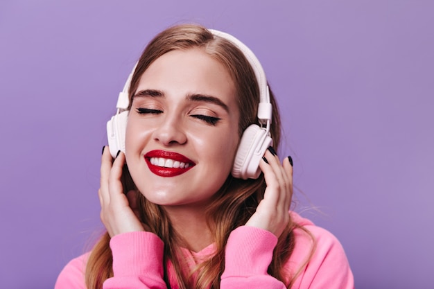 Ładna kobieta z czerwonymi ustami, uśmiechająca się i ciesząca się muzyką w słuchawkach