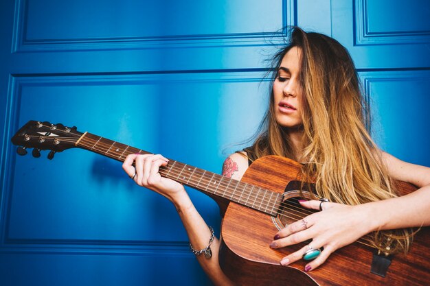Ładna kobieta z gitarą blisko błękit ściany