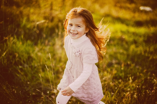 Ładna mała dziewczynka z czerwonymi włosami bawi się opadniętymi liśćmi