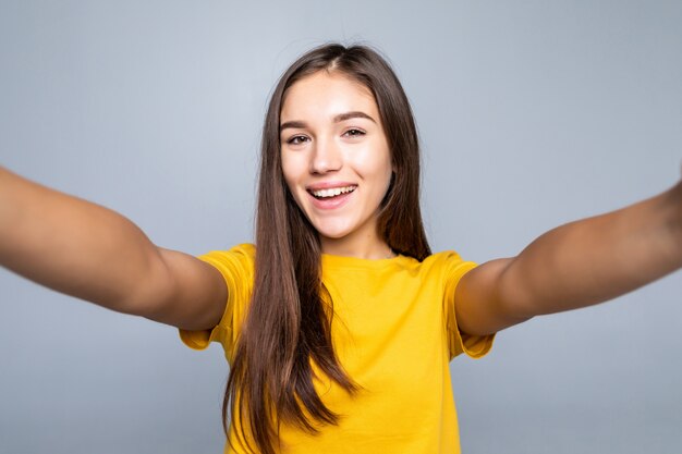 Ładna młoda kobieta robi selfie na biel ścianie