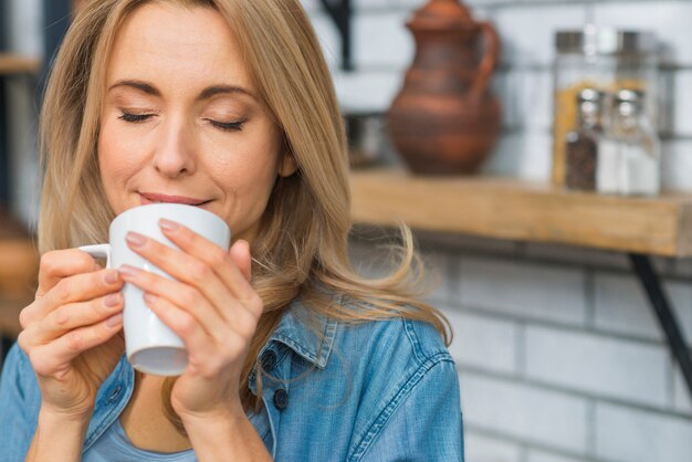 Ładna młoda kobieta wącha aromat jej kawowy napój