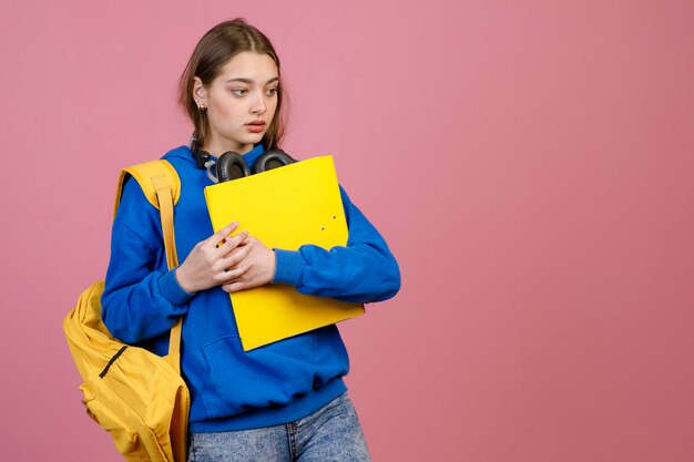 Ładna studentka stojąca trzymająca żółty plecak i folder