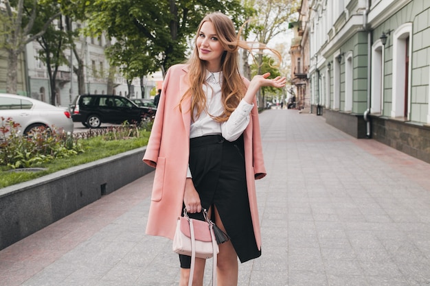 Ładny atrakcyjny stylowy uśmiechnięta kobieta spaceru ulicą miasta w różowym płaszczu