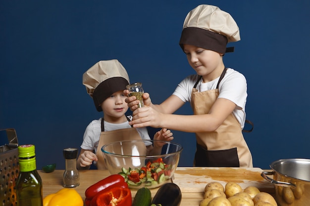 ładny mały chłopiec w kapeluszu kucharz stojący przy kuchennym stole