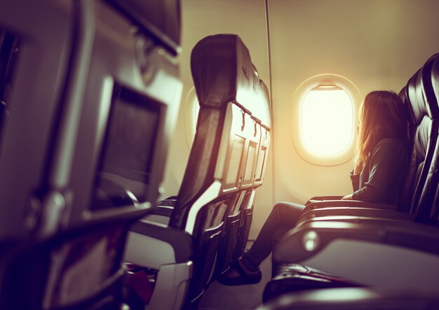 Lady siedzi w samolocie patrząc na błyszczące słońce przez okno