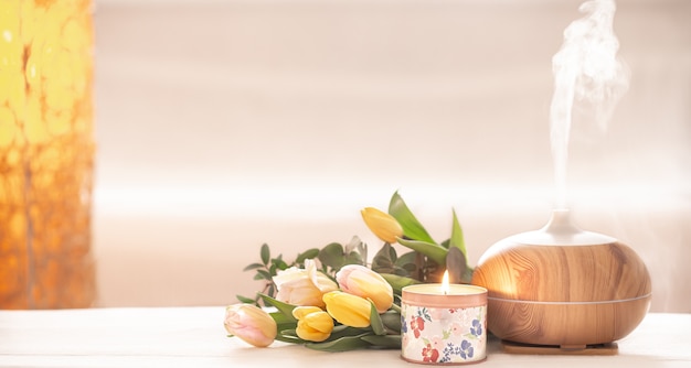 Lampa z dyfuzorem olejku aromatycznego na stole na rozmytym tle z pięknym wiosennym bukietem tulipanów i płonącą świecą.