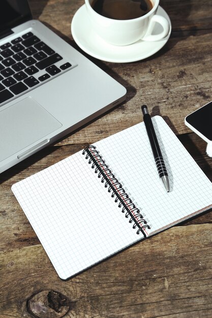 Laptop, notatnik i długopis na stole przy filiżance kawy