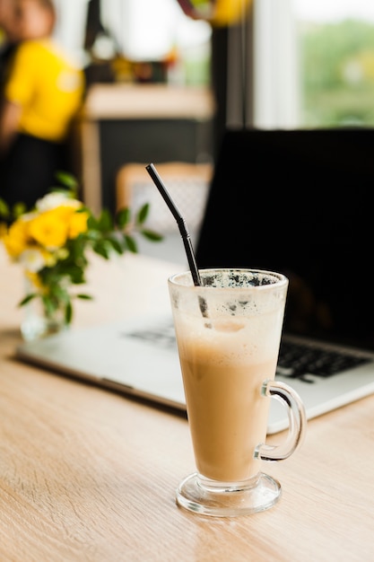 Latte filiżanka kawy ze słomką przed defocus laptopa na stole