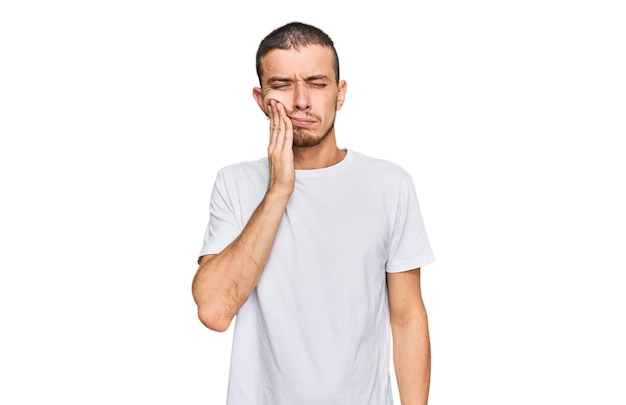 Latynos młody mężczyzna ubrany w swobodną białą koszulkę dotykający ust ręką z bolesnym wyrazem twarzy z powodu bólu zęba lub choroby zębów. dentysta