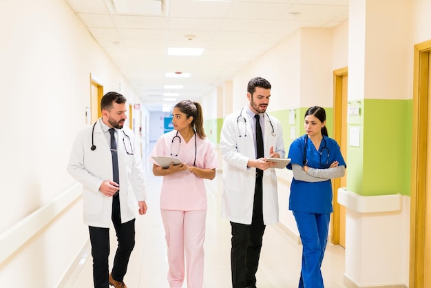 Bezpłatne zdjęcie latynoscy pracownicy służby zdrowia płci męskiej i żeńskiej omawiają raporty podczas spaceru korytarzem w szpitalu