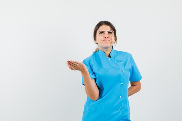 Lekarka podnosząca rękę w pytający sposób w niebieskim mundurze i wyglądająca na zirytowaną