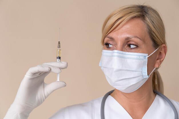 Lekarka z maską medyczną trzymającą strzykawkę ze szczepionką
