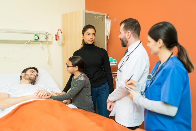 Lekarz i pielęgniarka wyjaśniają kobiecie chorobę stojąc przy chorym mężczyźnie w szpitalu