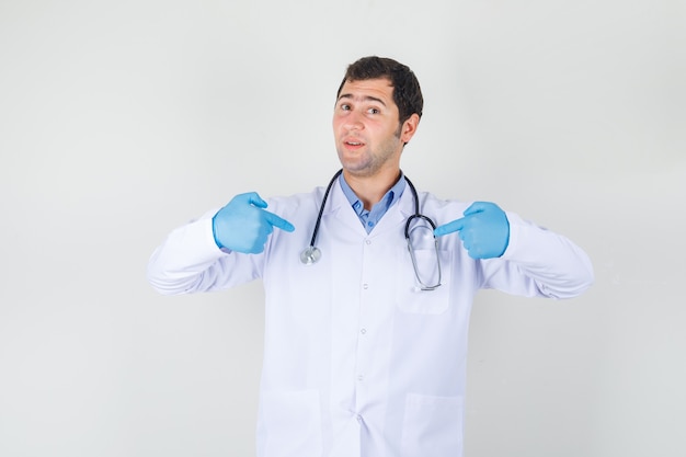 Lekarz mężczyzna wskazując palcami na siebie w białym fartuchu, rękawiczkach i patrząc dumnie. przedni widok.