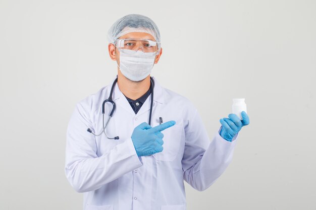 Lekarz mężczyzna wskazując palcem na butelkę pigułki w odzieży ochronnej i patrząc ostrożnie