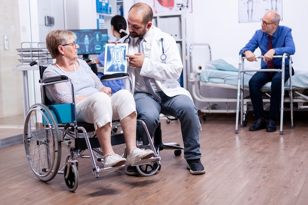 Lekarz pokazujący obraz rentgenowski mózgu niepełnosprawnej starszej starszej kobiety na wózku inwalidzkim