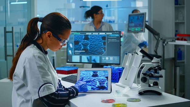 Lekarz technik laboratoryjny analizujący ewolucję wirusa patrząc na cyfrowy tablet. Zespół naukowców zajmujących się opracowywaniem szczepionek przy użyciu zaawansowanych technologii do badania leczenia pandemii Covid19.