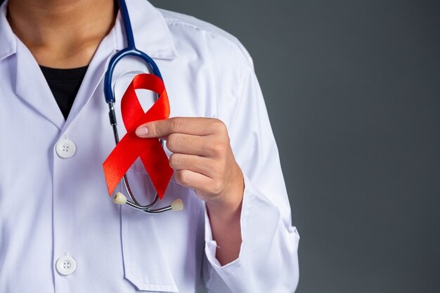 Lekarz trzyma czerwoną wstążkę, świadomość HIV, Światowy Dzień AIDS i Światowy Dzień Zdrowia Seksualnego.