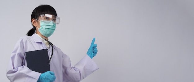 Lekarz w mundurze wskazuje na pusty obszar. noszenie niebieskich medycznych rękawiczek lateksowych, przezroczystych okularów i zielonej maski n95, aby zapobiec epidemii wirusa. azjatycki lekarz. gest ręki. stetoskop medyczny. książka o wirusach