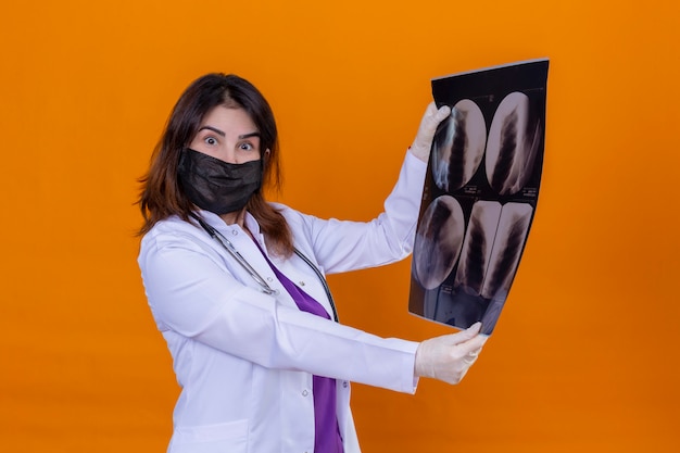 Bezpłatne zdjęcie lekarz w średnim wieku, ubrany w biały fartuch, w czarną maskę ochronną ze stetoskopem, trzymając prześwietlenie płuc