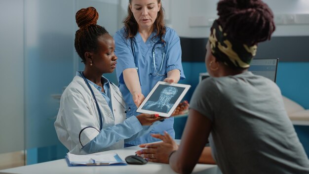 Lekarz wyjaśniający skanowanie rentgenowskie na tablecie do chorego pacjenta w gabinecie lekarskim. Medyk pokazujący diagnozę radiograficzną na urządzeniu cyfrowym do badania opieki zdrowotnej kobiecie z chorobą.