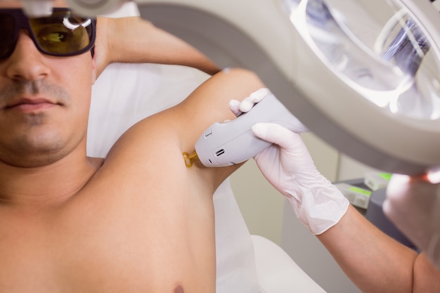 Lekarz wykonujący laserowe usuwanie owłosienia na męskiej skórze pacjenta