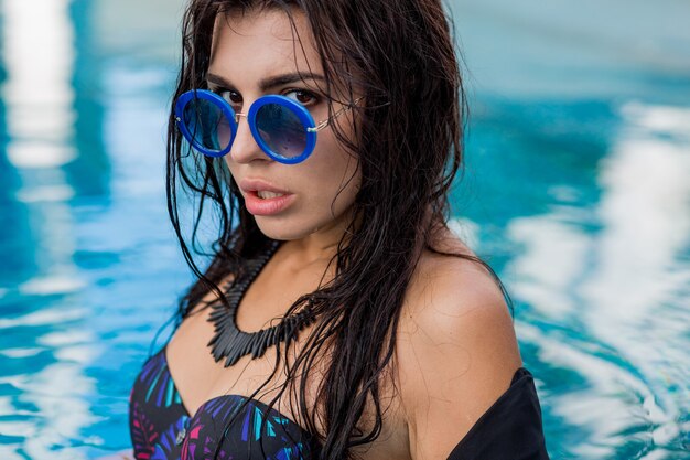 Letni portret pięknej seksownej modelki w czarnych strojach kąpielowych i stylowy naszyjnik pozowanie w basenie. Wakacje i tropikalny nastrój.