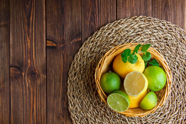 Limonki z cytrynami, zioła w wiklinowym koszu na drewnianym stole