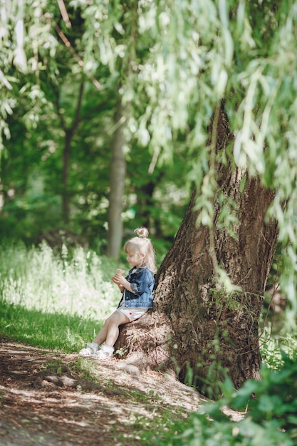 Little blond dziewczyna siedzi na drzewie jedzenie lodów