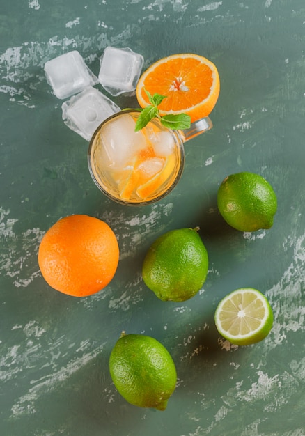 Bezpłatne zdjęcie lodowata woda detoksykacyjna w filiżance z pomarańczami, miętą, limonkami płasko leżała na gipsowej powierzchni