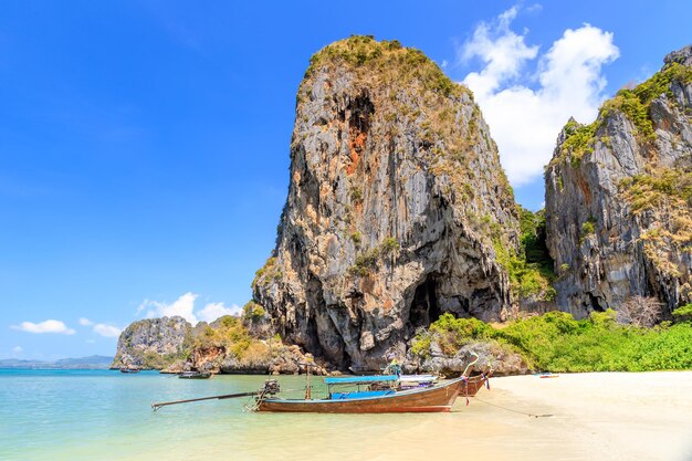 Łódź z długim ogonem i turkusowa, krystalicznie czysta woda morska z wapiennym klifem i górą na plaży Phra Nang, Krabi, Tajlandia