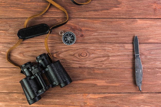 Bezpłatne zdjęcie lornetki, kompas i nóż na drewniane biurko