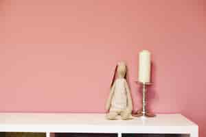 Bezpłatne zdjęcie loth zabawka królik i świeca na srebrnym świeczniku na białej półce na różowej ścianie