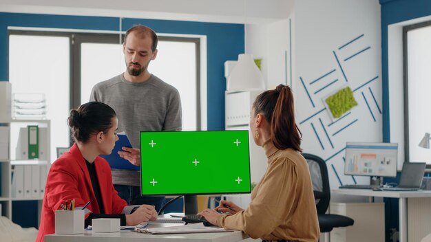 Ludzie biznesu pracujący na komputerze z zielonym ekranem w biurze uruchamiania. Koledzy wykonujący pracę zespołową i dyskutujący o izolowanym kluczu chrominancji z szablonem makiety i tłem na wyświetlaczu.
