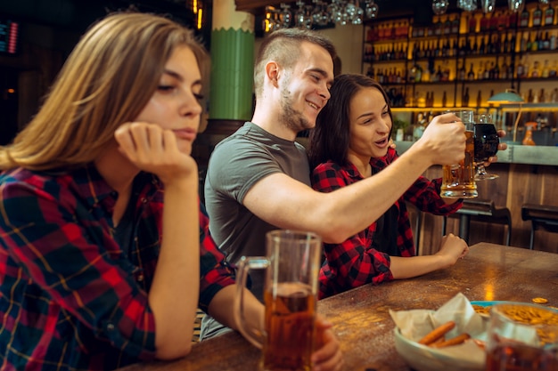 Ludzie, czas wolny, przyjaźń i komunikacyjny pojęcie, - szczęśliwi przyjaciele pije piwo, opowiada i brzęka szkła przy barem lub pubem