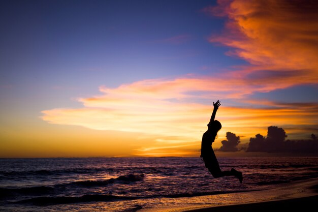 ludzie na plaży o zachodzie słońca. dziewczyna skacze