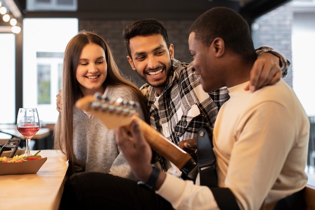 Ludzie uśmiechający się i obserwujący mężczyznę grającego na gitarze na imprezie
