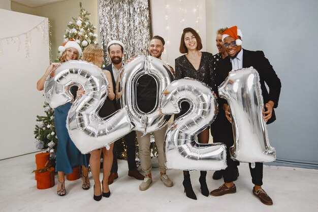 Ludzie w dekoracjach bożonarodzeniowych. Mężczyzna w czarnym garniturze. Grupowe obchody Nowego Roku. Ludzie z balonami 2021.