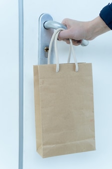 Ludzka ręka próbuje otworzyć zamknięte drzwi, a na jego nadgarstku wisi papierowa torba z jedzeniem.